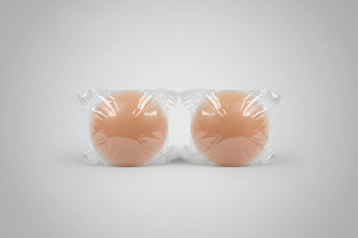 Two silicone breast forms wrapped in clear plastic on a textured surface.