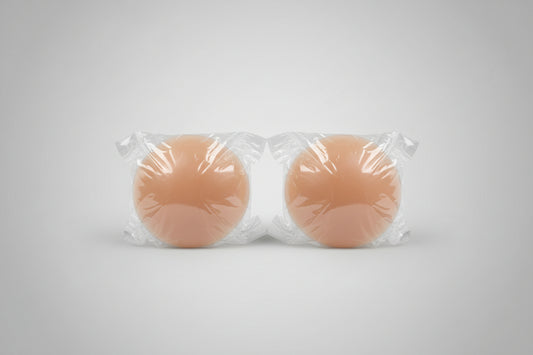 Two silicone breast forms wrapped in clear plastic on a textured surface.